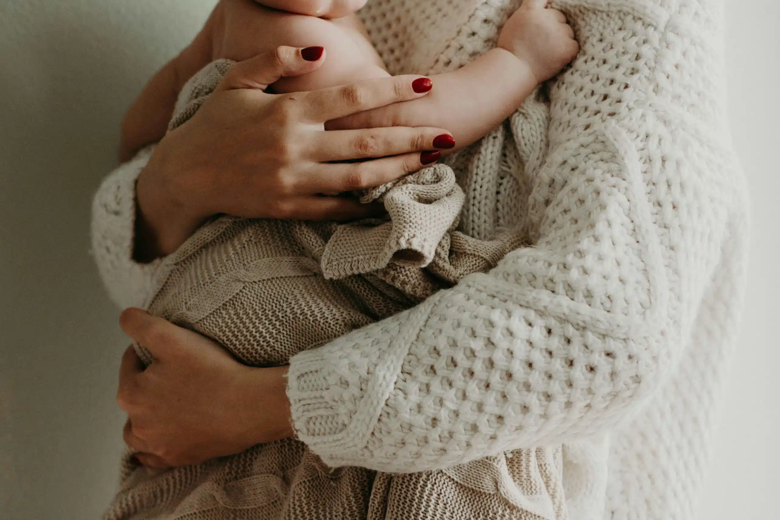 A mother gently holding her newborn wrapped in a cozy knit blanket, representing nurturing and warmth, symbolizing Postpartum care in Bronx, NY.