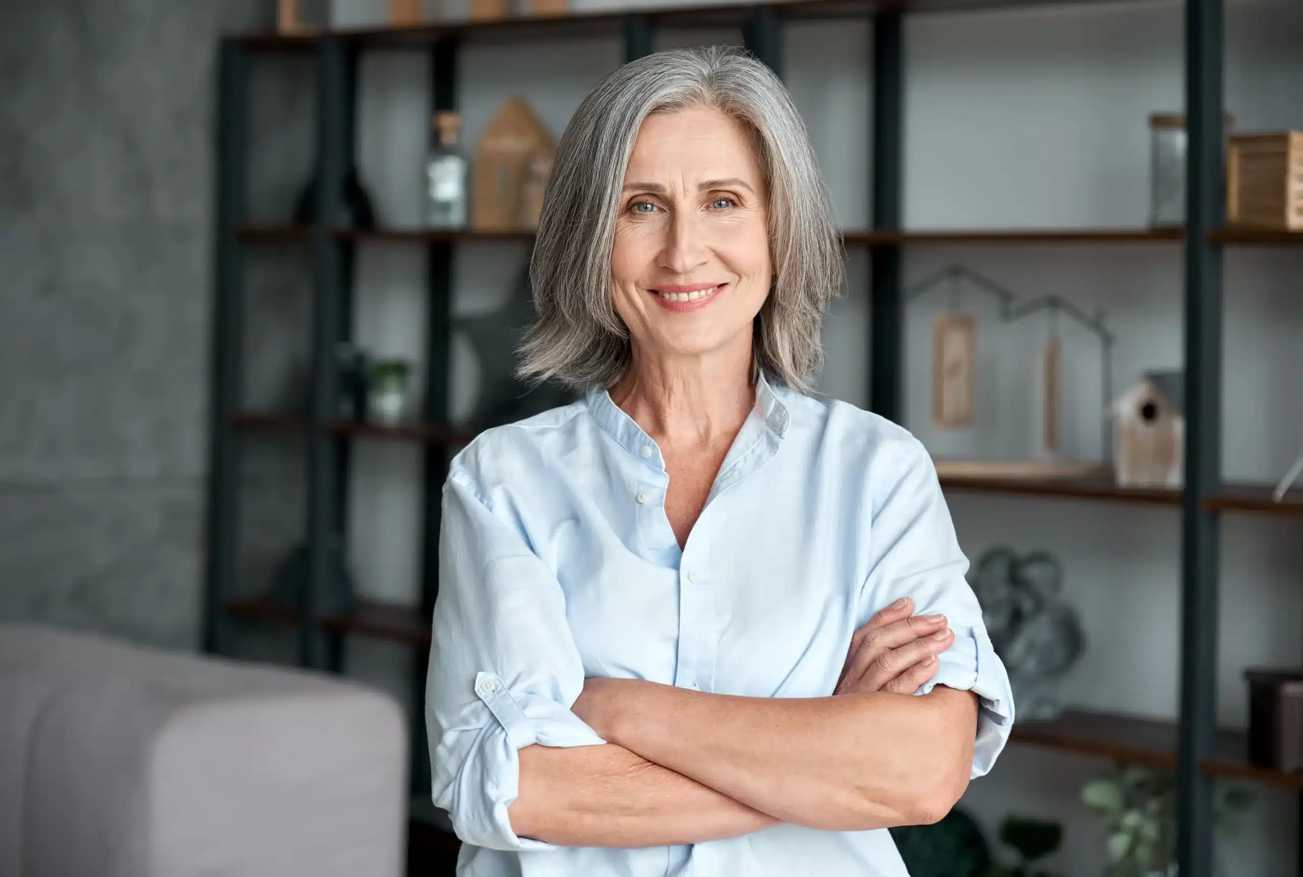 This photo shows a confident older woman with gray hair and a soft smile, standing with arms crossed. She reflects strength during perimenopause vs menopause.