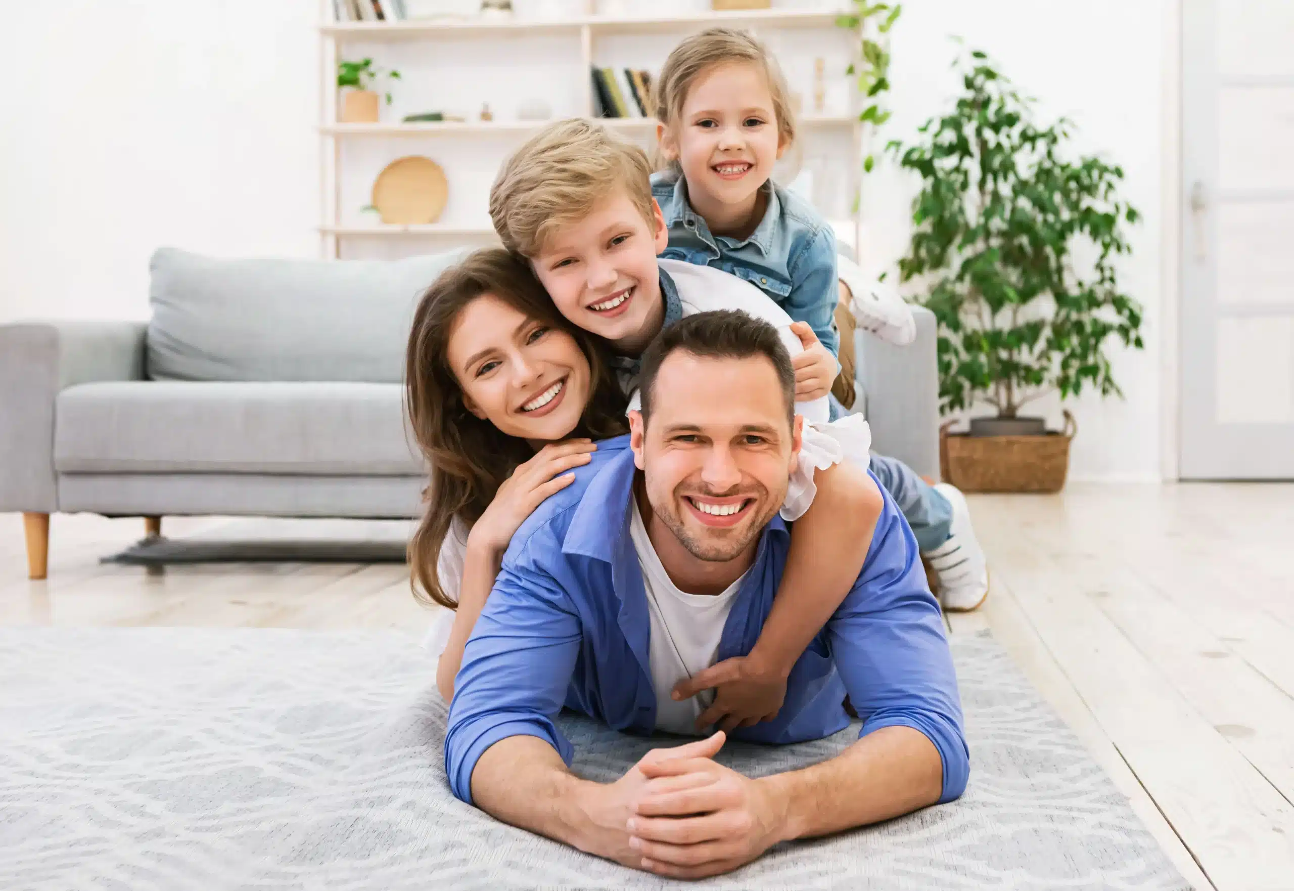 A happy family of four smiling and stacked playfully on the floor in a bright living room, representing the kind of care and connection supported by a trusted family physician in the Bronx.