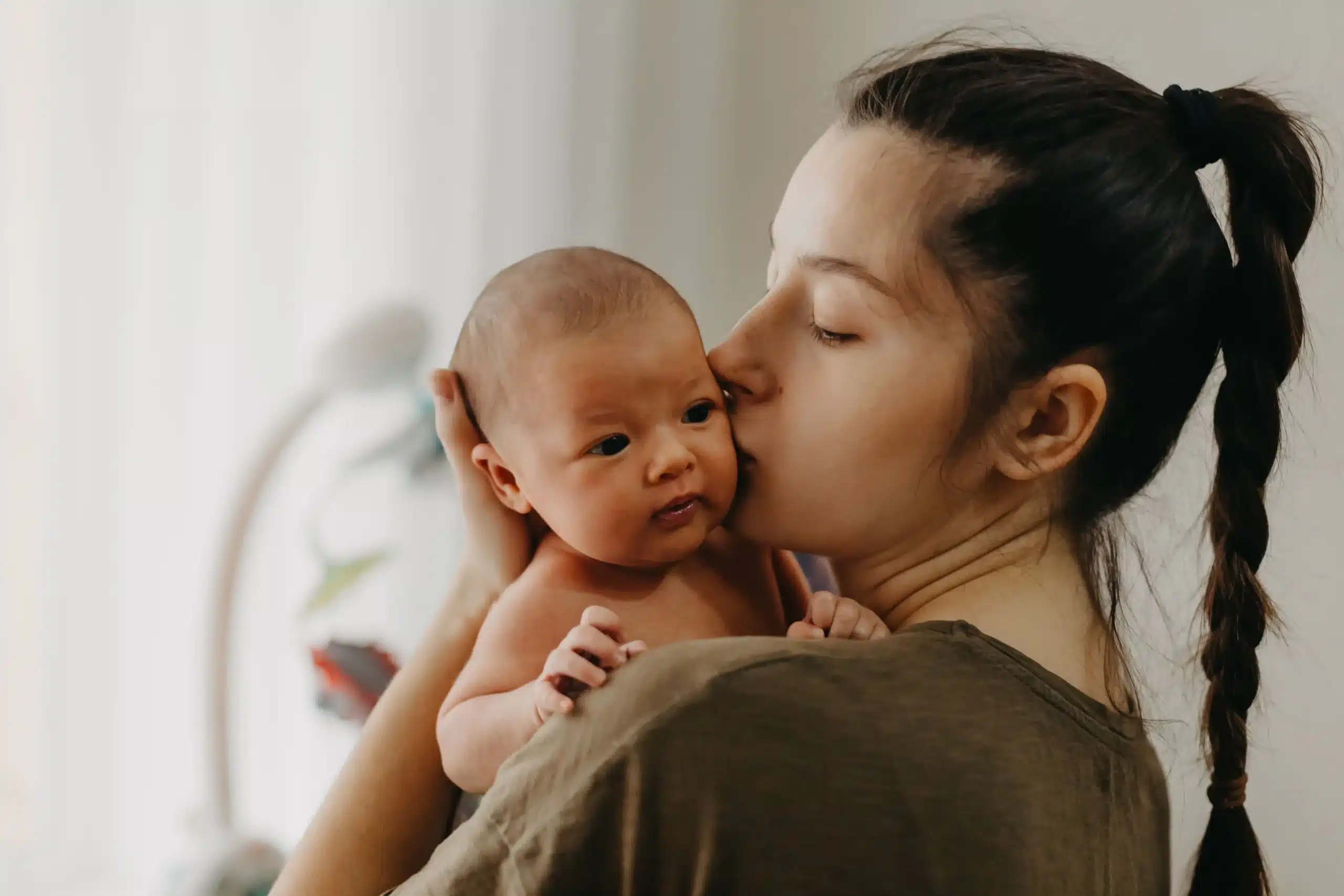 A mother gently kissing her newborn baby's cheek, highlighting the essential bond supported by Bronx Healthy Start postpartum care.